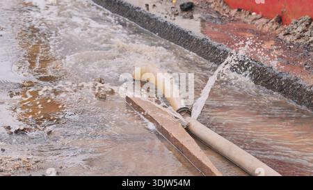 Inonder la rue avec de l'eau jaillissant d'un tuyau posé sur le sol Banque D'Images