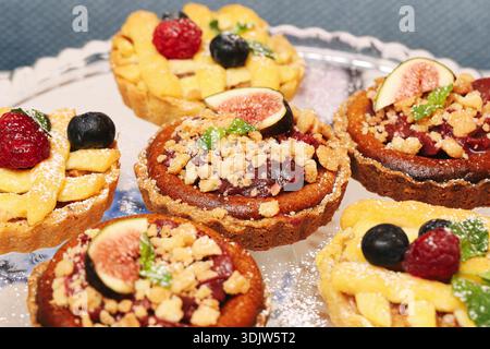 Tartelettes aux fruits faites maison aux figues, framboises et bleuets servies sur une assiette en verre. Pâtisseries sucrées cuites au four avec garniture de crumble préparées pour le dessert. Banque D'Images