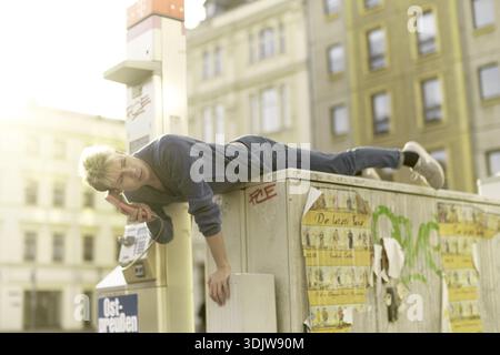 Jeune homme tendu accroché au téléphone dans la ville de Cottbus, Brandebourg, Allemagne, Un jeune homme se penche avec désinvolture contre une cabine téléphonique de la ville dans un setti urbain Banque D'Images