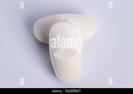 comprimés oblongs blancs avec texture granulaire empilés sur la surface mate, vue macro rapprochée révèle un revêtement poudreux et une forme compacte, adaptés aux supplemen Banque D'Images