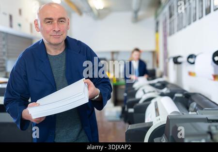 Portrait d'un employé de la maison d'impression avec pile de papier dans ses mains Banque D'Images