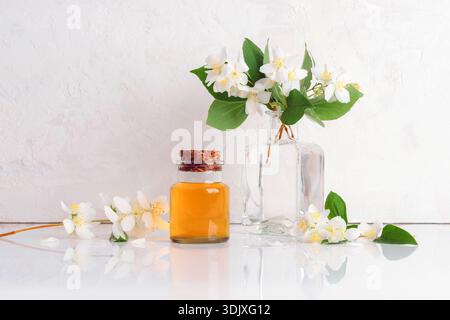 Bouteille en verre avec de l'huile dorée et des fleurs de jasmin blanc sur fond texturé clair. Concept d'aromathérapie. Banque D'Images
