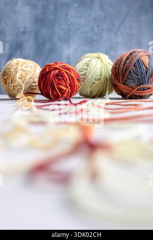 Photographie rapprochée de quatre boules de fil multicolores disposées en rangée sur un fond doux et texturé. La faible profondeur de champ met en évidence les fibres Banque D'Images