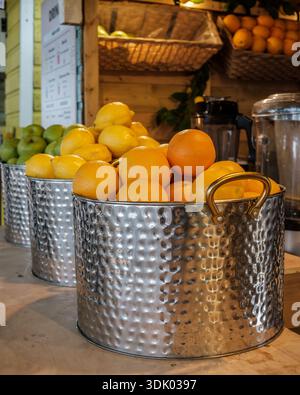 Oranges fraîches et pommes vertes exposées dans des seaux en métal dans un stand de jus de fruits de rue, prêt pour des boissons fraîchement pressées. Banque D'Images