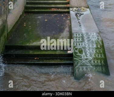 Marches en pierre près de la Tamise avec des marques à la craie et de petits rochers, partiellement submergés par l'eau de marée de la rivière à Londres. Banque D'Images