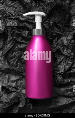 Bouteille à pompe de shampooing rose fuchsia sur papier d'emballage froissé noir Banque D'Images