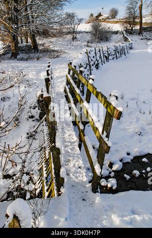 Un pont en bois recouvert de neige sur long Preston Beck (pont Scalehaw) mène au-delà d'une ferme (sur la droite) puis vers le village de long Preston. Banque D'Images