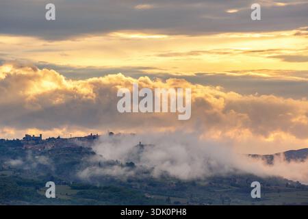 Village sur une colline avec des nuages dans un coucher de soleil Banque D'Images