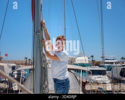 Femme marin tient le tissu de voile blanc se préparant à lever des voiles sur le yacht. L'activité physique et les compétences de manœuvre de bateau sont montrées pendant la préparation à l'as Banque D'Images