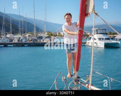 Femme marin tient le tissu de voile blanc se préparant à lever des voiles sur le yacht. L'activité physique et les compétences de manœuvre de bateau sont montrées pendant la préparation à l'as Banque D'Images