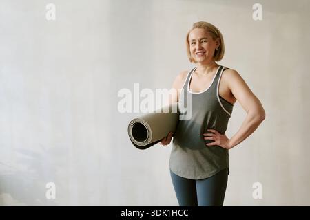 Femme d'âge moyen souriant tout en tenant Yoga Mat à l'intérieur Banque D'Images
