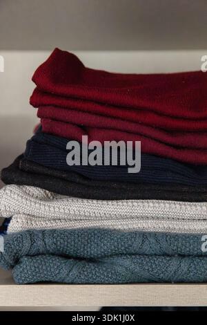 Pile de pulls en tricot pliés de différentes couleurs soigneusement disposés sur une étagère, mettant en évidence les textures confortables et le rangement organisé de la garde-robe Banque D'Images