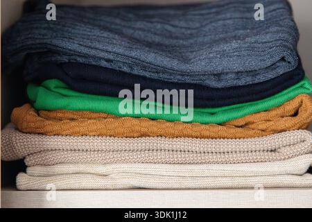 Pile de pulls en tricot pliés de différentes couleurs soigneusement disposés sur une étagère, mettant en évidence les textures confortables et le rangement organisé de la garde-robe Banque D'Images