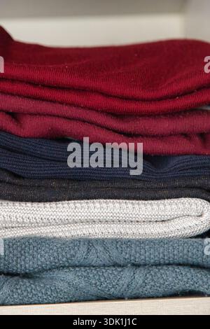Pile de pulls en tricot pliés de différentes couleurs soigneusement disposés sur une étagère, mettant en évidence les textures confortables et le rangement organisé de la garde-robe Banque D'Images