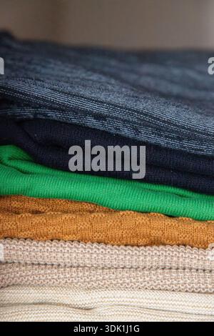 Pile de pulls en tricot pliés de différentes couleurs soigneusement disposés sur une étagère, mettant en évidence les textures confortables et le rangement organisé de la garde-robe Banque D'Images