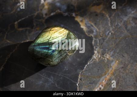 Pierre précieuse unique en labradorite polie photographiée sur une surface de marbre sombre avec une lumière directionnelle spectaculaire et une ombre profonde. Banque D'Images