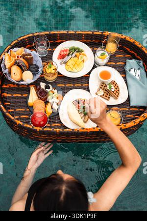 Vue aérienne d'une femme appréciant un petit déjeuner dans la piscine flottante Banque D'Images