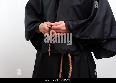 Gros plan de mains de moine avec chapelet en robe noire, isolé Banque D'Images