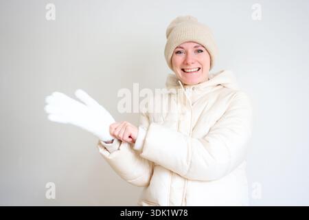 Heureuse jeune femme mettant des gants blancs habillés de vêtements d'hiver confortables à l'intérieur Banque D'Images