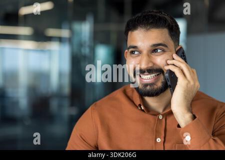 Homme avec une barbe souriant brillamment tout en conversant sur un téléphone mobile, représentant une communication réussie, la technologie et l'interac d'affaires positif Banque D'Images