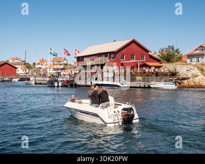 Bateau à moteur passant devant le restaurant du port de Knuts Brygga sur le front de mer dans le village de Mollösund, archipel de Bohuslän, côte ouest de la Suède Banque D'Images