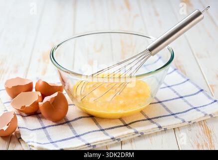 le processus de cuisson de l'omelette, gros plan. Cuisiner des œufs frais brouillés pour le petit déjeuner. oeufs crus avec un bol d'oeufs cassés et fouet pour la cuisson . Banque D'Images