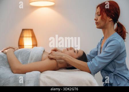 Cosmétologie, nettoyage de la peau du visage. Jeune femme détendue se faisant masser par un thérapeute dans un salon de spa. Banque D'Images