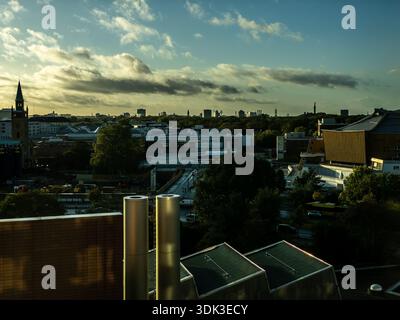 Vue panoramique à l'heure dorée sur les toits de Berlin avec flèches d'église, cheminées industrielles et tours modernes silhouettes sur un vaste ciel nuageux Banque D'Images