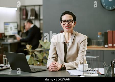 Portrait d'une femme d'âge moyen souriant tout en étant assise au bureau Banque D'Images