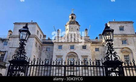 Une grande façade ensoleillée d'un bâtiment historique de la ville avec une tour de l'horloge centrale, une porte voûtée et des clôtures complexes en fer forgé. L'imposant a Banque D'Images