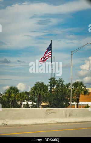 Un drapeau américain seul coupe l'air lourd et humide au-dessus d'une autoroute à Panama City, en Floride. Vue d'une voiture qui passe, la scène est un aperçu éphémère Banque D'Images