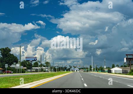 La lumière du soleil traverse des nuages spectaculaires et lourds, projetant une lumière vive et à fort contraste sur une large autoroute vide à Panama City, en Floride. L'air est th Banque D'Images