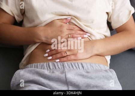 Femme tenant l'estomac dans la douleur gros plan. Crampes abdominales et concept de problème digestif. Soins de santé et gêne menstruelle à l'intérieur. Banque D'Images
