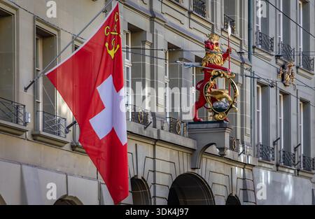 Un drapeau suisse rouge flotte devant une façade médiévale ornée d'une statue de lion dorée dans l'Altstadt ou la vieille ville de Berne, en Suisse Banque D'Images