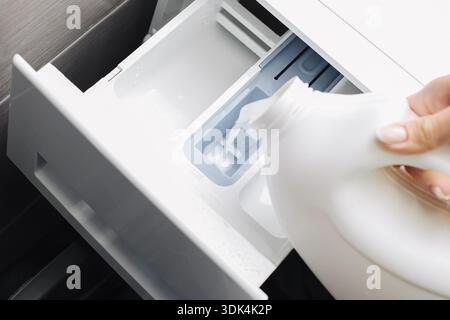 Verser la lessive liquide dans le tiroir du lave-linge avant le cycle de lavage. Processus de préparation du linge ménager axé sur l'entretien des tissus et le nettoyage à la maison Banque D'Images