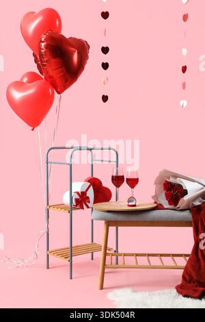 Banc gris avec des verres de vin, des roses et des décorations pour la célébration de la Saint-Valentin sur fond rose Banque D'Images