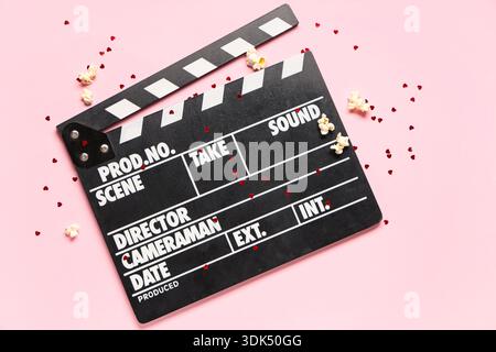 Film clapper avec pop-corn et confettis sur fond rose. Fête de la Saint-Valentin Banque D'Images