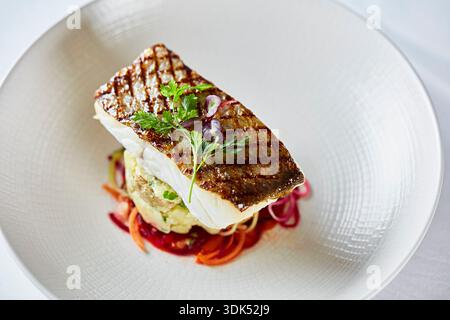 Filet de bar grillé sur un lit de pommes de terre et de légumes Banque D'Images