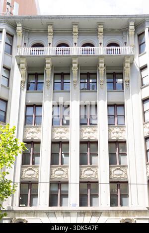 Une façade de bâtiment de couleur crème avec un balcon, des fenêtres cintrées, des panneaux décoratifs et de nombreuses fenêtres rectangulaires encadrées de bois sombre. Banque D'Images