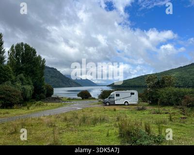 Un camping-car stationné à côté d'un fjord pittoresque près de Puyuhuapi dans le sud du Chili, entouré de montagnes boisées et d'eaux côtières calmes. Le déplacement du véhicule de loisirs Banque D'Images