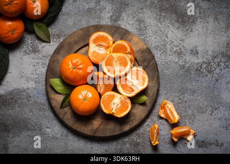 Fruits de mandarines juteux et sains ou mandarines sur fond gris. Fruits entiers et moitiés dans une assiette en bois Banque D'Images