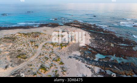 Vue aérienne de la côte rocheuse et des dunes de sable rencontrant l'océan turquoise sous la douce lumière du jour Banque D'Images