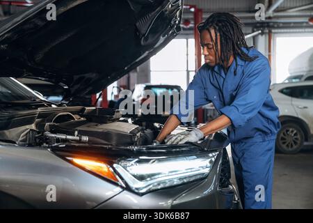 La partie avant, le capot est ouvert, fixant l'automobile. Mécanicien masculin est avec voiture dans le garage. Banque D'Images
