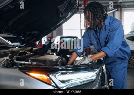 La partie avant, le capot est ouvert, fixant l'automobile. Mécanicien masculin est avec voiture dans le garage. Banque D'Images