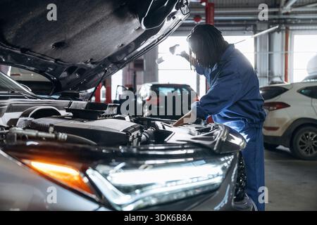 La partie avant, le capot est ouvert, fixant l'automobile. Mécanicien masculin est avec voiture dans le garage. Banque D'Images