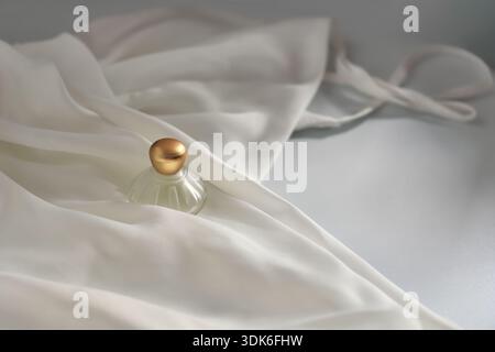 Élégante bouteille de parfum féminine plate lay closeup sur robe blanche en soie Banque D'Images