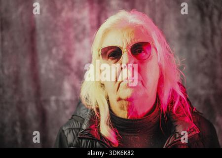 Portrait d'une femme caucasienne de soixante-dix ans portant des lunettes de soleil. Une légère réflexion d'une lumière LED rouge arrive sur le visage de la femme Banque D'Images