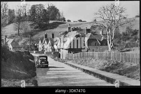 En regardant vers le nord le long de Sandhill Close, montrant les numéros 49-56, avec une voiture à moteur au premier plan, et l'église St Michael sur la colline en arrière-plan, Millbrook, Central Bedfordshire, 1940-1960. Le bâtiment au toit de chaume vu au premier plan de cette image, le numéro 56, a depuis été démoli et remplacé par une maison moderne. Banque D'Images