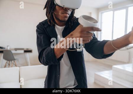 Jeu de tir, contrôleurs de maintien. Homme noir dans des lunettes de réalité virtuelle à la maison. Banque D'Images
