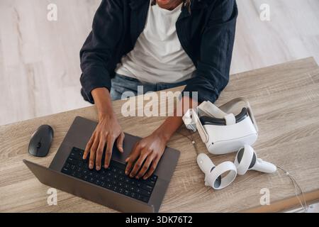 Le jeune homme est assis à table avec un ordinateur portable et des lunettes de réalité virtuelle. Banque D'Images